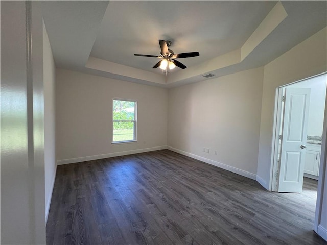 empty room with dark hardwood / wood-style flooring, ceiling fan, and a tray ceiling