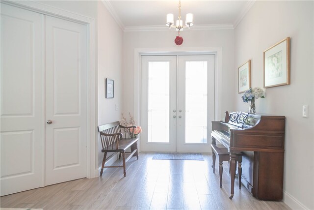 foyer entrance with ornamental molding, french doors, light hardwood / wood-style floors, and a chandelier