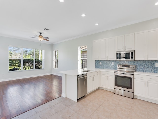 kitchen featuring stainless steel appliances, white cabinets, kitchen peninsula, ornamental molding, and light wood-type flooring