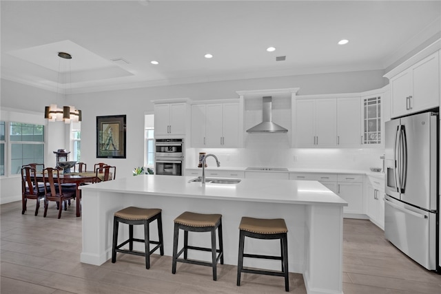 kitchen featuring stainless steel appliances, white cabinetry, sink, wall chimney exhaust hood, and an island with sink