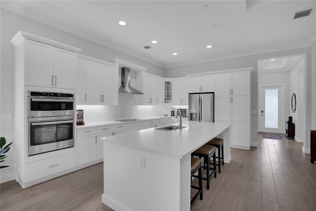 kitchen with white cabinets, sink, a kitchen island with sink, wall chimney range hood, and appliances with stainless steel finishes