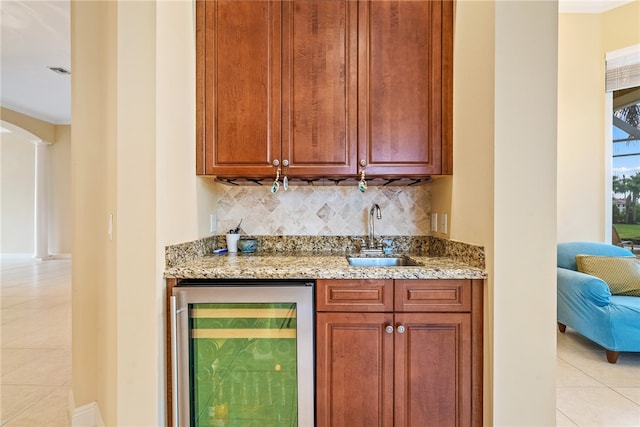 bar featuring backsplash, light tile patterned floors, light stone countertops, sink, and beverage cooler