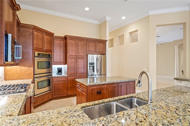 kitchen with a center island, sink, ornamental molding, light stone countertops, and appliances with stainless steel finishes