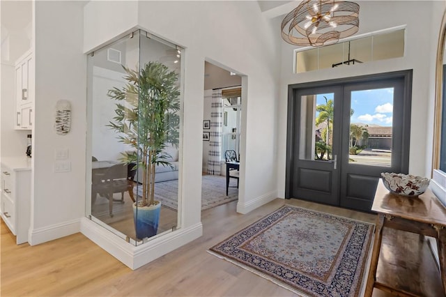 foyer entrance featuring a chandelier, french doors, wood-type flooring, and a high ceiling