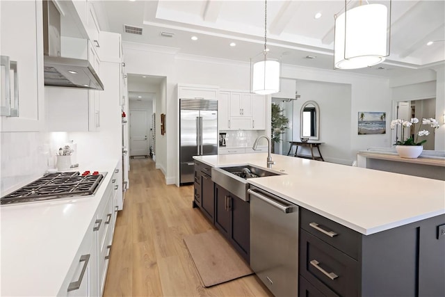 kitchen featuring sink, white cabinetry, hanging light fixtures, stainless steel appliances, and wall chimney exhaust hood