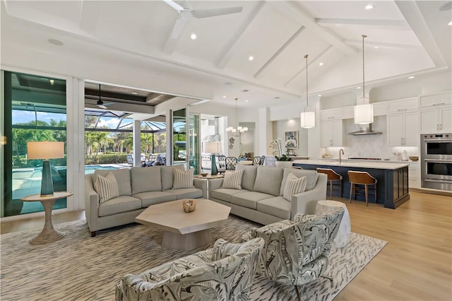 living room with ceiling fan, beam ceiling, sink, and light wood-type flooring