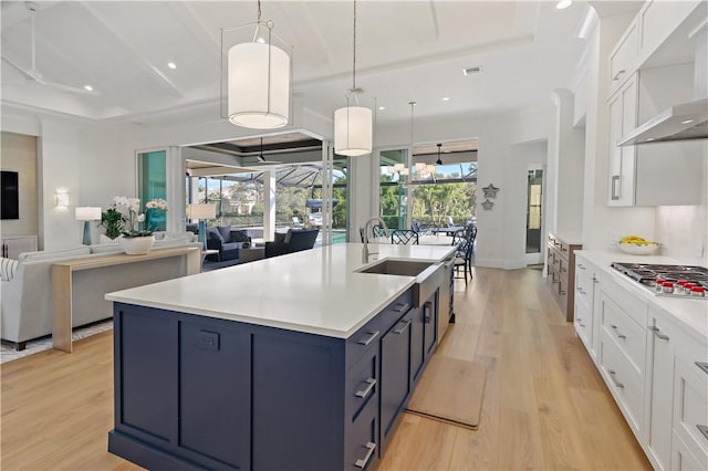 kitchen featuring pendant lighting, wall chimney range hood, white cabinets, blue cabinets, and stainless steel gas stovetop