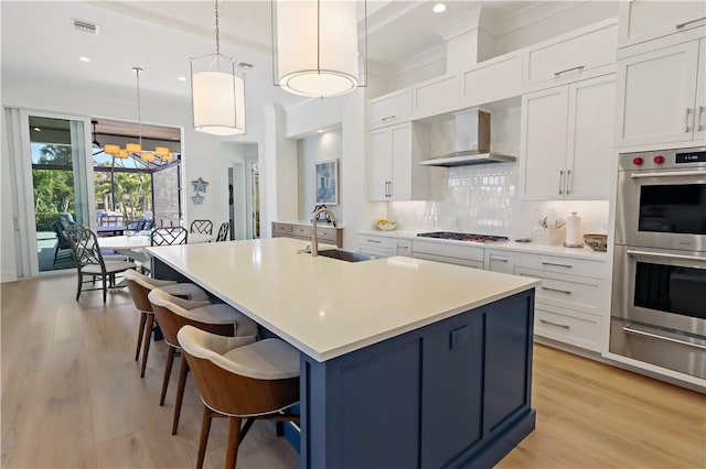 kitchen with decorative light fixtures, white cabinetry, sink, and wall chimney exhaust hood