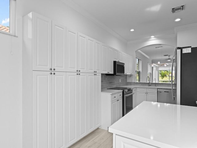 kitchen with crown molding, kitchen peninsula, stainless steel appliances, decorative backsplash, and white cabinets