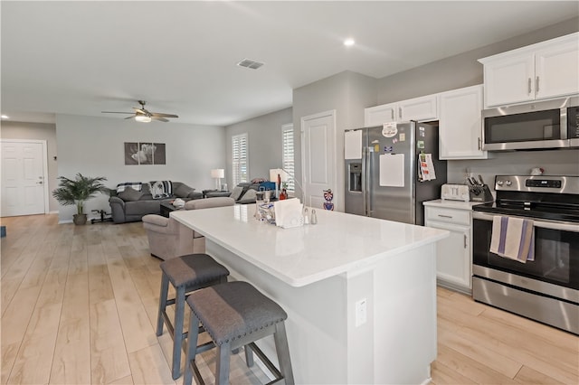 kitchen with appliances with stainless steel finishes, a kitchen bar, a center island, white cabinets, and light wood-type flooring