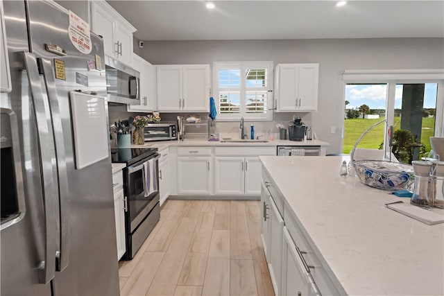 kitchen featuring light stone counters, white cabinetry, appliances with stainless steel finishes, sink, and light hardwood / wood-style flooring