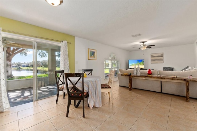 dining area with light tile patterned floors, ceiling fan, and a water view