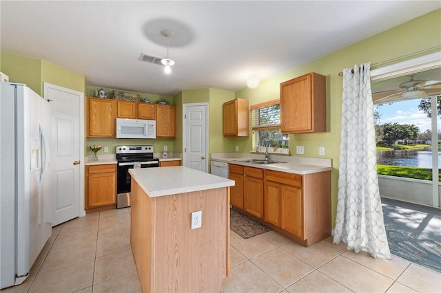 kitchen with white appliances, a center island, sink, and light tile patterned floors