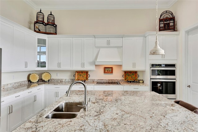 kitchen with pendant lighting, custom exhaust hood, sink, black electric cooktop, and stainless steel double oven