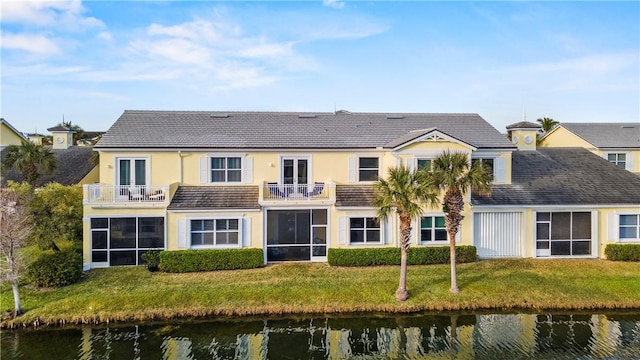 back of property with a balcony, a water view, and a yard