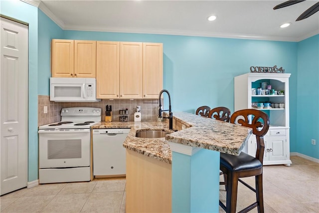 kitchen with sink, white appliances, a breakfast bar area, light stone countertops, and kitchen peninsula