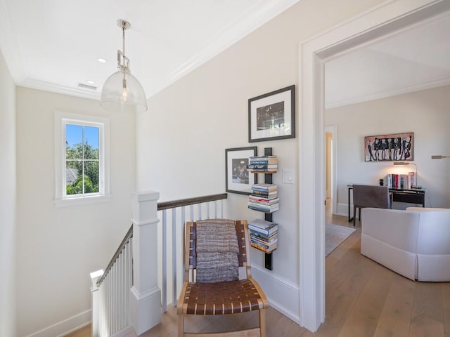 corridor with baseboards, visible vents, ornamental molding, light wood-style floors, and an upstairs landing