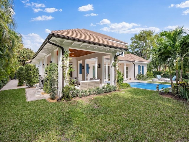 rear view of house featuring a patio, a tiled roof, and a lawn