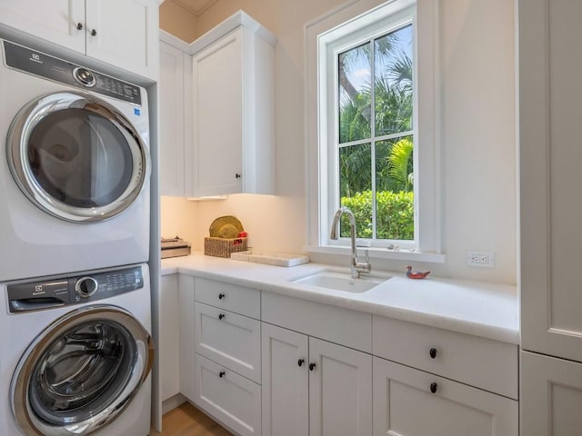 washroom featuring cabinet space, stacked washer / drying machine, and a sink