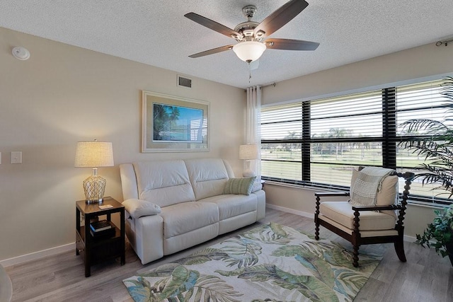 living room with ceiling fan, light wood-type flooring, and a textured ceiling