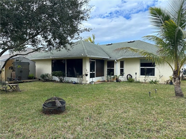 back of house featuring an outdoor fire pit, a lawn, a sunroom, and a storage shed