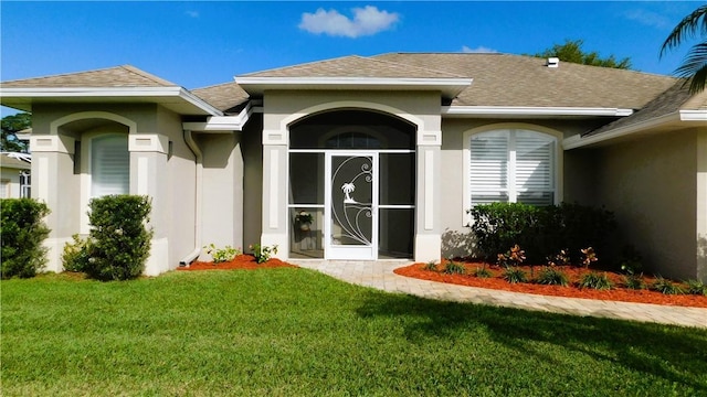 doorway to property featuring a shingled roof, a lawn, and stucco siding