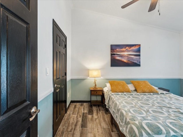 bedroom featuring wood finished floors, crown molding, lofted ceiling, baseboards, and a ceiling fan