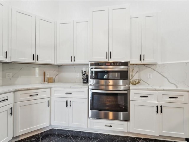 kitchen featuring double oven, dark marble finish floors, white cabinets, decorative backsplash, and light stone counters
