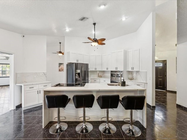 kitchen featuring appliances with stainless steel finishes, light countertops, tasteful backsplash, a ceiling fan, and a kitchen bar