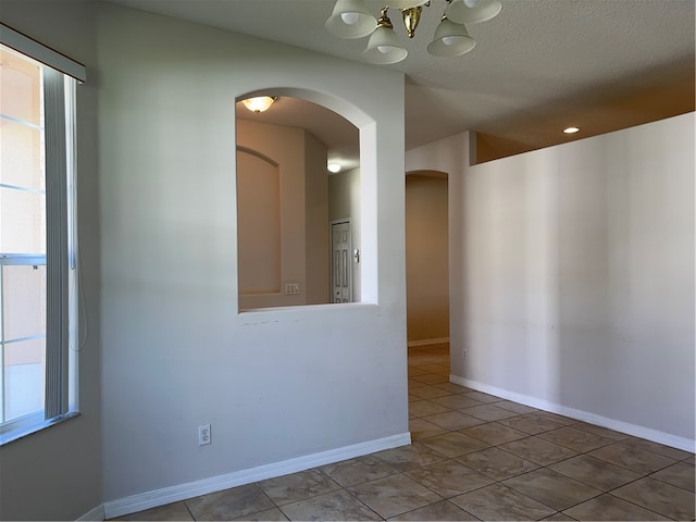 tiled empty room with an inviting chandelier, plenty of natural light, and a textured ceiling