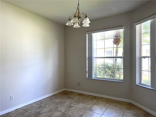 unfurnished room featuring a textured ceiling, light tile patterned floors, and an inviting chandelier