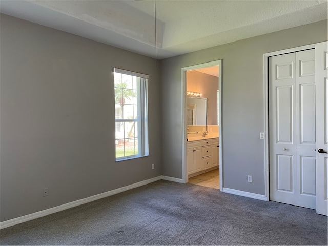 unfurnished bedroom with light colored carpet, ensuite bath, a closet, and a textured ceiling