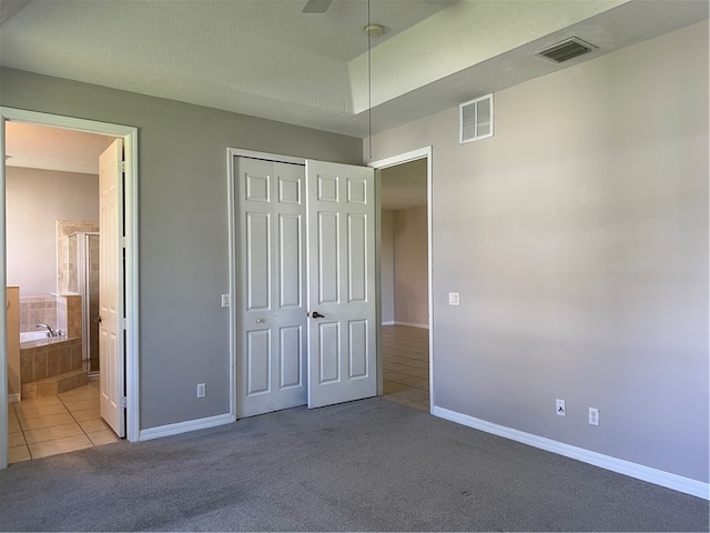 unfurnished bedroom with a closet, a textured ceiling, light colored carpet, ceiling fan, and ensuite bathroom