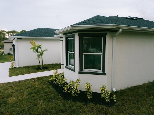 view of property exterior featuring stucco siding, a yard, and a shingled roof