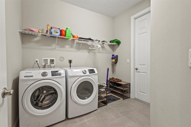 laundry room featuring washing machine and clothes dryer, a textured ceiling, and light tile patterned floors