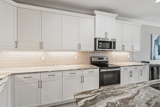 kitchen with light stone counters, ornamental molding, backsplash, white cabinetry, and appliances with stainless steel finishes