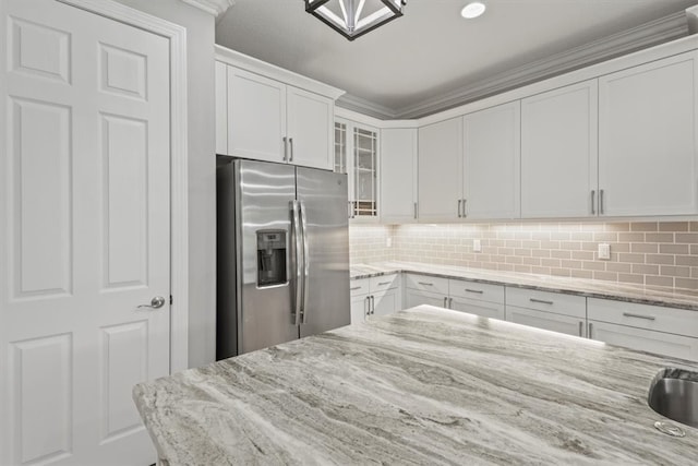 kitchen featuring white cabinetry, stainless steel refrigerator with ice dispenser, ornamental molding, and light stone counters