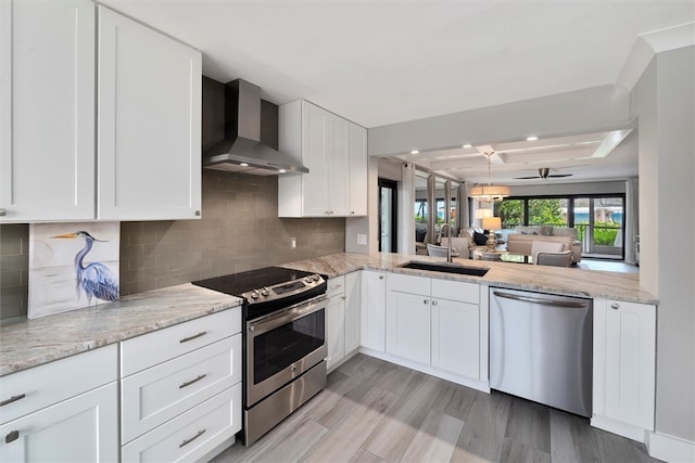 kitchen featuring stainless steel appliances, white cabinetry, sink, light hardwood / wood-style flooring, and wall chimney range hood