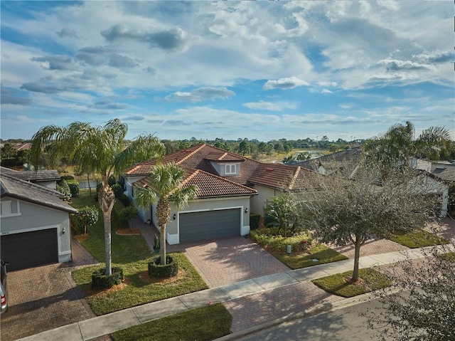 mediterranean / spanish-style home featuring a tiled roof, decorative driveway, an attached garage, and stucco siding