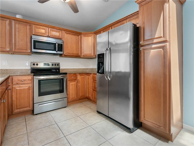 kitchen featuring stainless steel appliances, light stone counters, vaulted ceiling, light tile patterned flooring, and ceiling fan