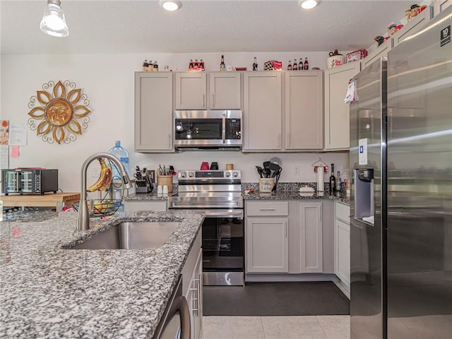 kitchen with appliances with stainless steel finishes, light stone counters, a textured ceiling, a sink, and light tile patterned flooring