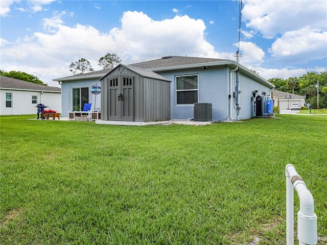 rear view of property with a lawn, central AC, and an outbuilding