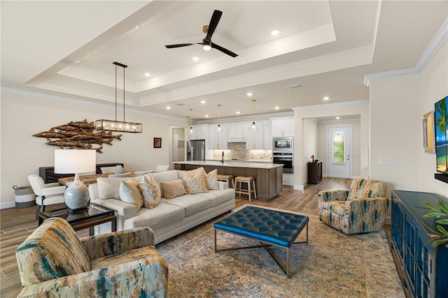 living room featuring crown molding, ceiling fan, a tray ceiling, and light hardwood / wood-style flooring