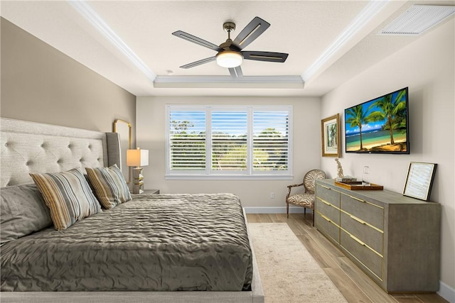 bedroom with crown molding, light hardwood / wood-style flooring, a raised ceiling, and ceiling fan