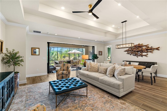 living room with hardwood / wood-style flooring, ceiling fan, a tray ceiling, and crown molding