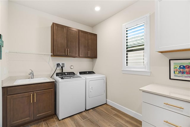 laundry area with cabinets, washing machine and dryer, sink, and light hardwood / wood-style flooring