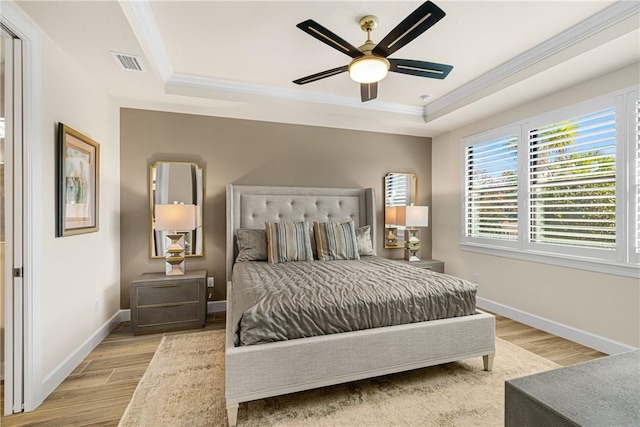 bedroom featuring crown molding, light hardwood / wood-style flooring, ceiling fan, and a tray ceiling