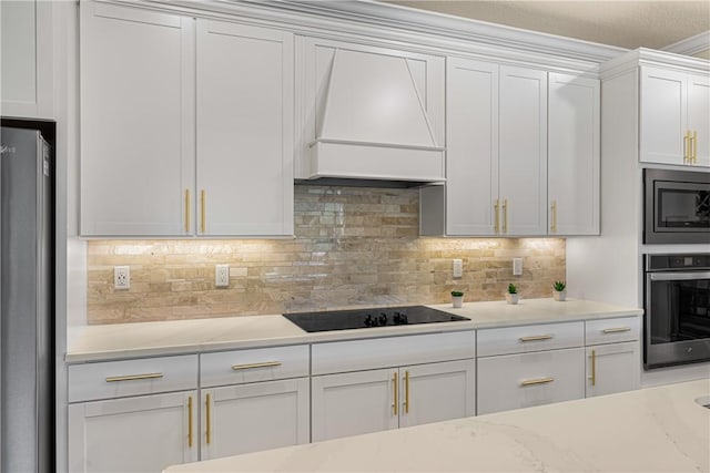 kitchen featuring premium range hood, light stone counters, white cabinets, stainless steel appliances, and backsplash