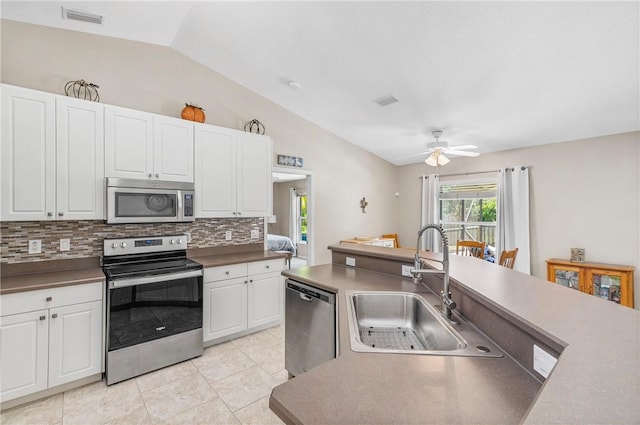 kitchen with a sink, vaulted ceiling, white cabinets, appliances with stainless steel finishes, and backsplash