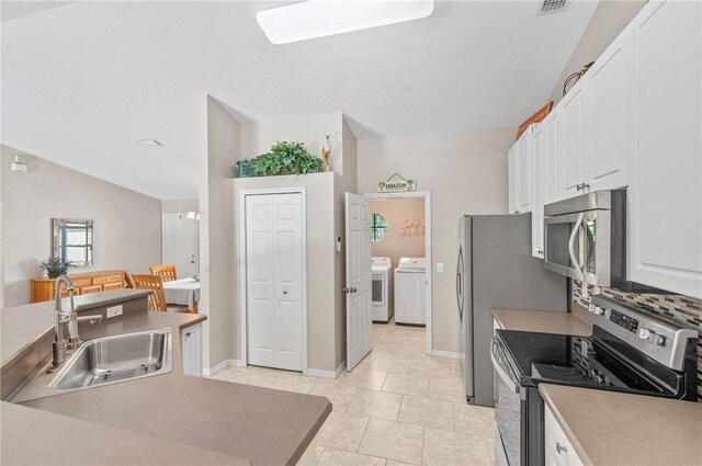 kitchen featuring lofted ceiling, a sink, stainless steel appliances, white cabinets, and independent washer and dryer